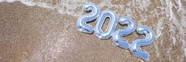 Silberne Ballons mit Zahlen, die auf Sand von Meernahaufnahmehintergrund liegen