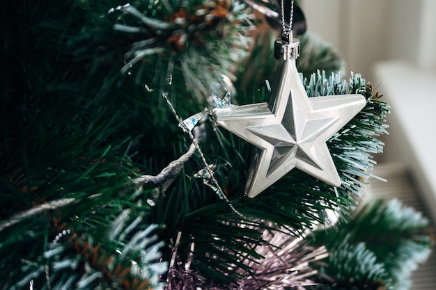 Silberner Stern und blassrosa Girlande auf künstlichem Weihnachtsbaum. Selektiver Fokus. Weihnachtskarte mit Dekoration für Silvester