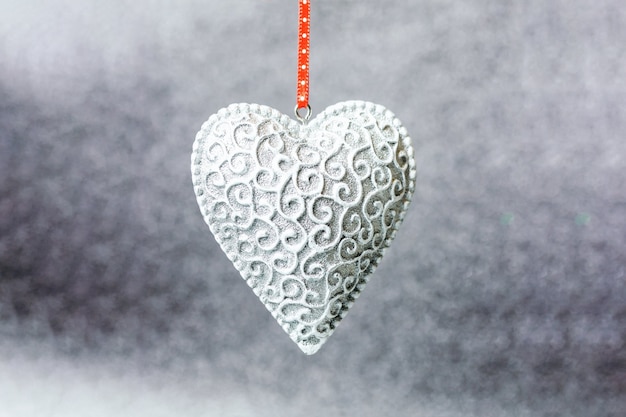 Silbernes Herz mit einem Muster auf einem verschwommenen, glänzenden Grau