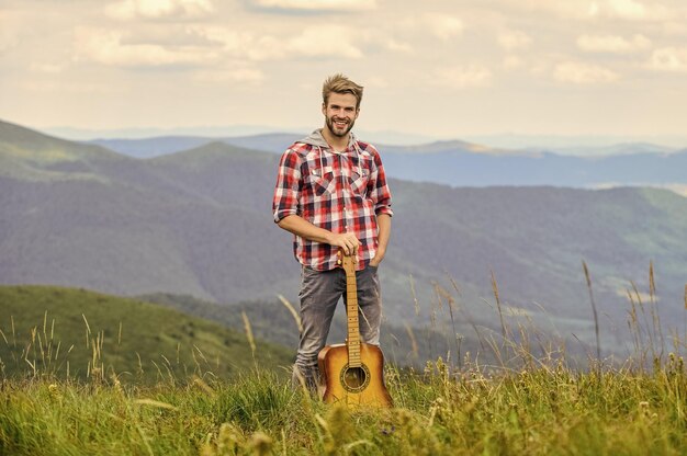 Silêncio das montanhas e som das cordas da guitarra Músico hipster Ambiente inspirador Músico homem com guitarra no topo da montanha Músico inspirado Festival de música de verão ao ar livre Tocando música