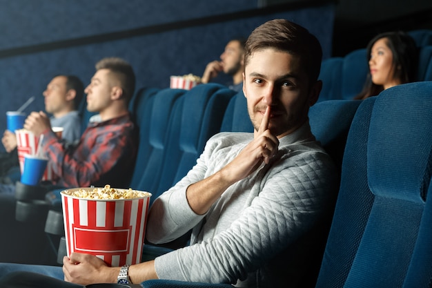 Silencio por favor. Varón joven haciendo gesto de silencio en el cine