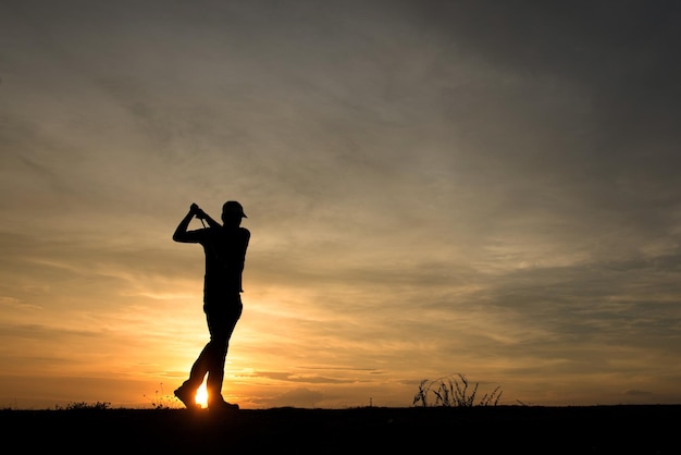 Silhouette asiatischer Golfspieler, der bei schönem Sonnenuntergang Golf spielt