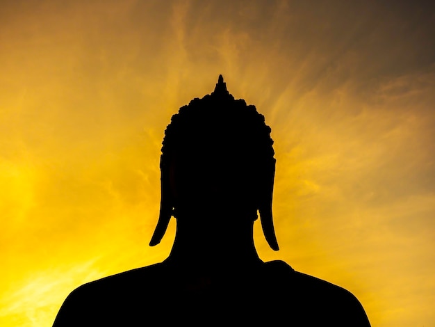 Silhouette der alten Buddha-Statue auf goldenem Sonnenuntergangshimmel im historischen Park Sukhothai, einem UNESCO-Weltkulturerbe in Thailand.