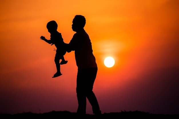 Silhouette der Familie, die der Vater mit dem Jungen glücklich mit dem Sonnenuntergangshimmel spielt