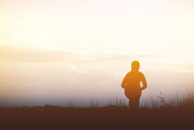 Silhouette der glücklichen jungen Frau, die gegen Sonnenuntergang in den Bergen springt