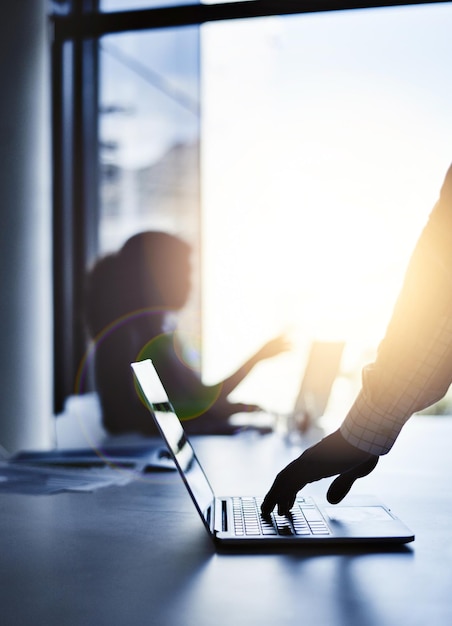 Silhouette der Hand eines Geschäftsmannes, der an einem Laptop in einem Büro mit Sonnenlicht und einem verschwommenen Schatten einer Frau im Hintergrund mit Bokeh arbeitet Umriss eines männlichen Brainstormings im Büro