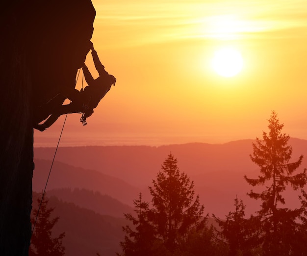 Silhouette des Bergsteigers, der an einer Klippe hängt Landschaft der Berggipfel, Sonnenschein im Hintergrund Über gefiltertem Kopierbereich