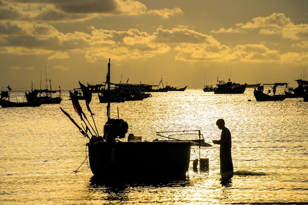 Silhouette des Fischers, der sein Netz bei Sonnenaufgang oder Sonnenuntergang am traditionellen Fischerboot auswirft Traditionelle Fischer bereiten das Fischernetz mit schönem Sonnenunterganghimmel vor