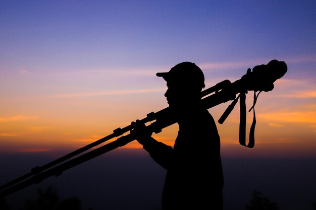 Silhouette des Fotografen mit Stativ Junger indischer Mann, der mit seiner Kamera fotografiert