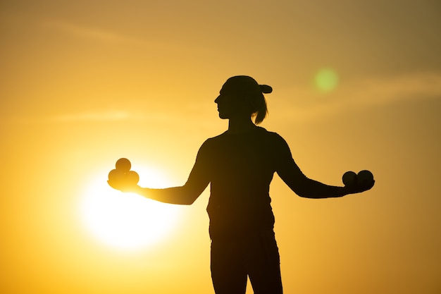 Silhouette des Jongleurs mit Bällen auf buntem Sonnenuntergang.