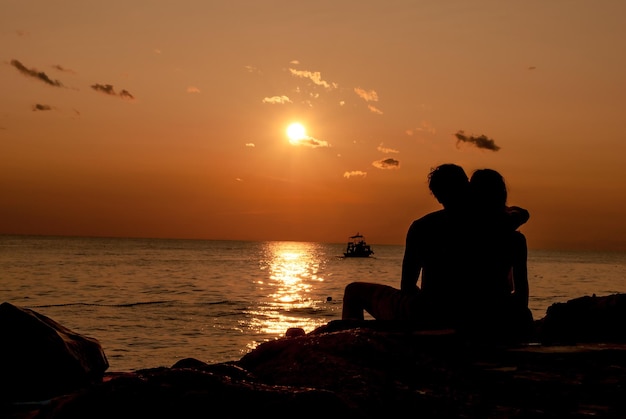 Silhouette ein liebevolles Paar sitzt bei Sonnenuntergang am Strand
