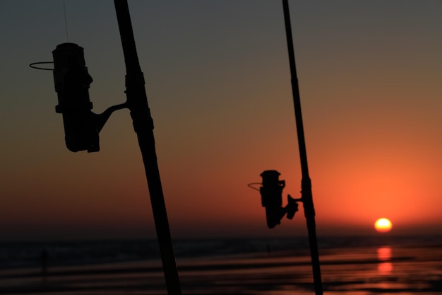 Silhouette einer Angelrute an einem Strand bei Sonnenuntergang