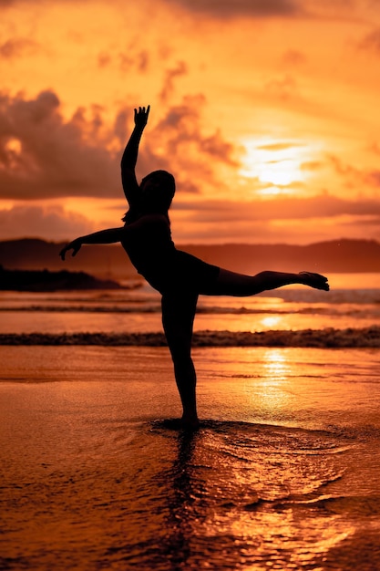 Silhouette einer asiatischen Frau, die mit großer Flexibilität und Blick auf die Wellen hinter ihr Ballett tanzt