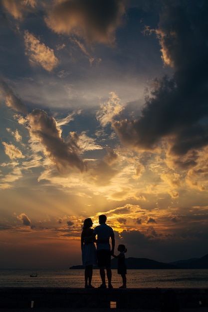 Silhouette einer Familie mit Kindern vor dem Hintergrund der untergehenden Sonne und des Meeres