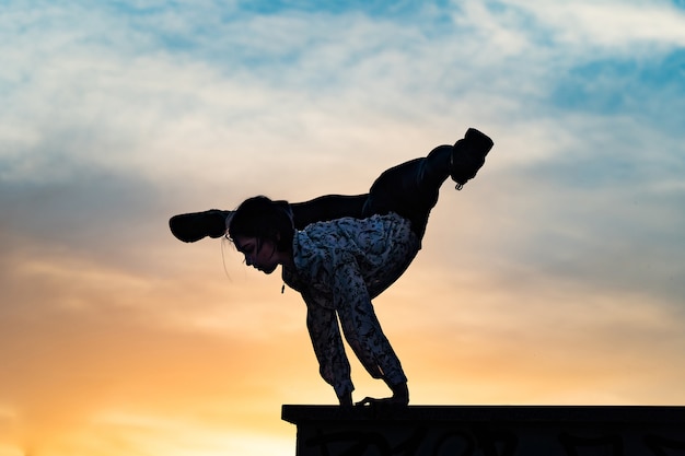 Silhouette einer flexiblen Zirkusartistin, die Handstand auf dem dramatischen Sonnenuntergangskonzept der einzelnen macht.