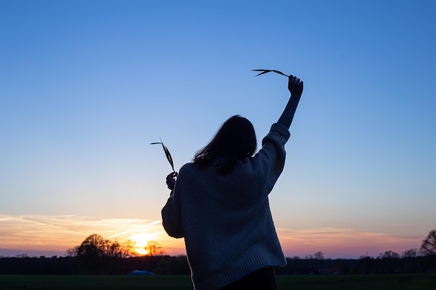 Silhouette einer Frau bei Sonnenuntergang auf einem Feld gegen die Rückansicht des Himmels