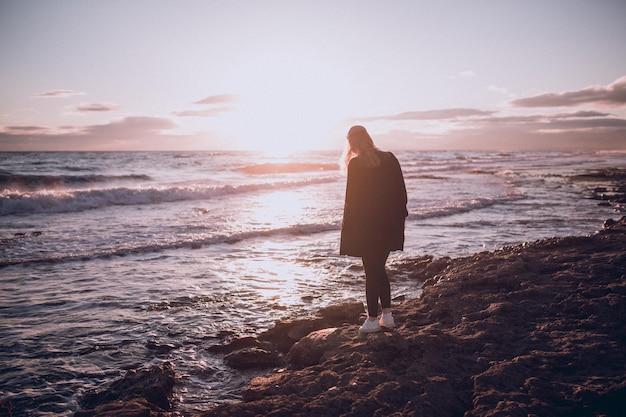 Silhouette einer Frau, die bei Sonnenuntergang am Strand steht