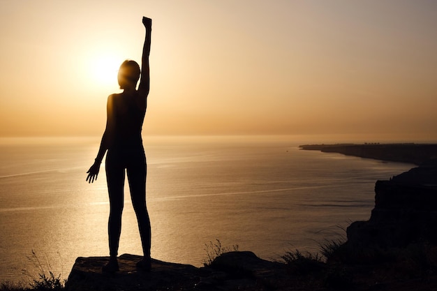 Silhouette einer Frau mit erhobenen Händen am Strand bei Sonnenuntergang