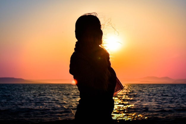 Silhouette einer Frau vor dem Hintergrund des Sonnenuntergangs am Meer Mädchen in einer Jacke auf dem Hintergrund von