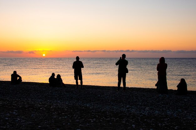 Silhouette einer Gruppe von Freunden, die im Sonnenuntergang am Strand stehen