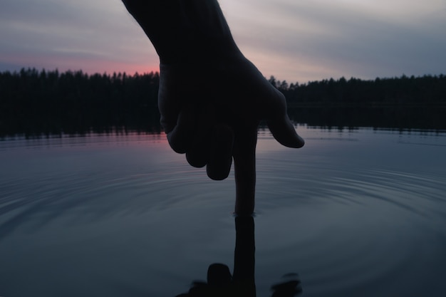 Silhouette einer Hand, die die Wasseroberfläche berührt. Menschlicher Einfluss auf die Umwelt