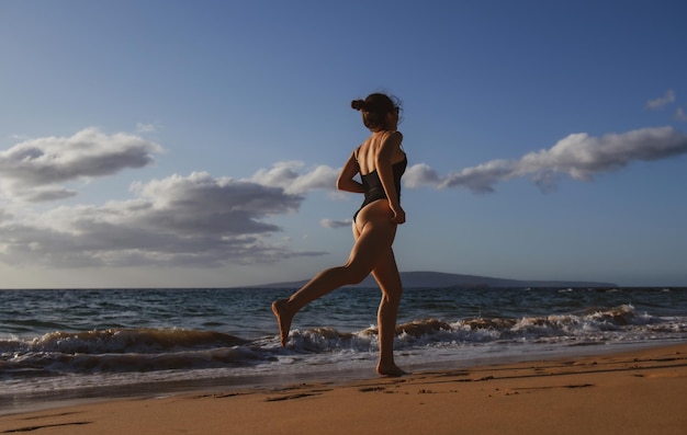 Silhouette einer jungen Frau, die am Strand des Meeres entlang läuft