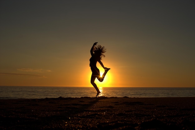 Foto silhouette einer jungen frau, die am strand tanzt