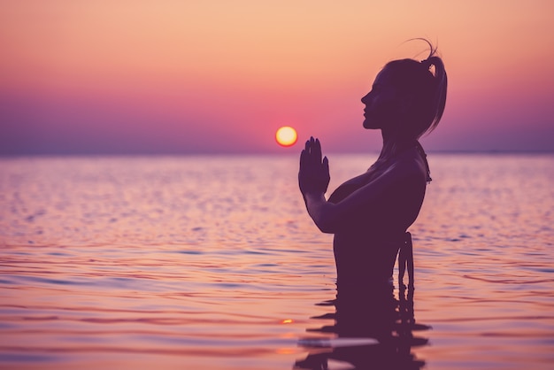 Silhouette einer jungen Frau, die bei Sonnenaufgang Yoga am Strand praktiziert