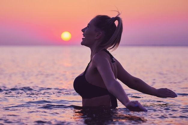 Silhouette einer jungen Frau, die bei Sonnenaufgang Yoga am Strand praktiziert