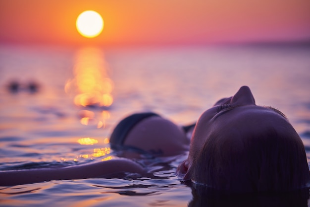 Silhouette einer jungen Frau, die bei Sonnenaufgang Yoga am Strand praktiziert