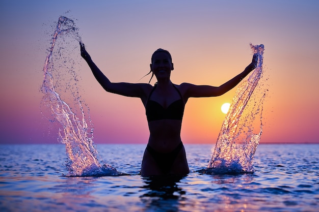 Silhouette einer jungen Frau, die bei Sonnenaufgang Yoga am Strand praktiziert