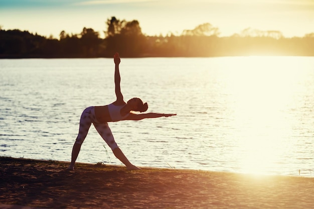 Silhouette einer jungen Frau, die bei Sonnenuntergang Yoga-Übungen am Seestrand macht