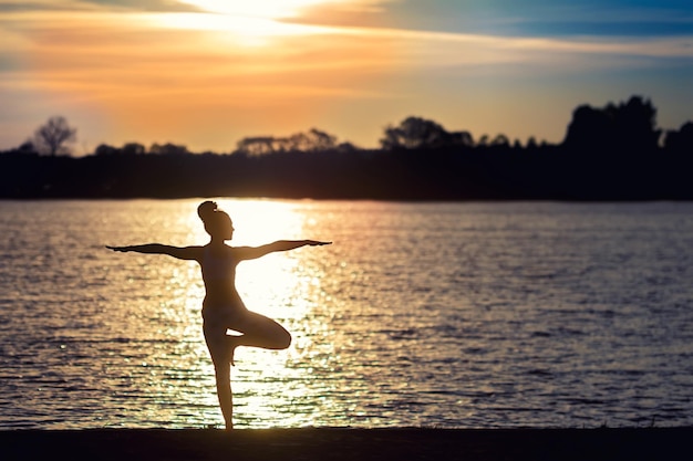 Silhouette einer jungen Frau, die bei Sonnenuntergang Yoga-Übungen am Seestrand macht