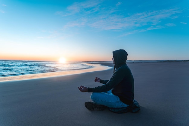 Silhouette einer Person am Ufer des Strandes, die bei Sonnenuntergang meditiert