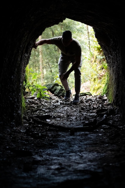 Silhouette einer Person, die eine kleine Höhle betritt Mann, der das Innere einer mysteriösen Höhle erkundet