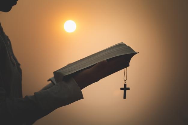 Silhouette einer Person, die während des Sonnenuntergangs ein Kreuz gegen den Himmel hält