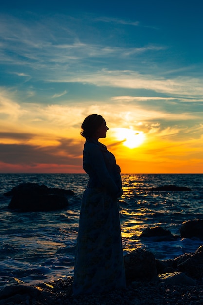 Silhouette einer schwangeren Frau bei Sonnenuntergang am Meer