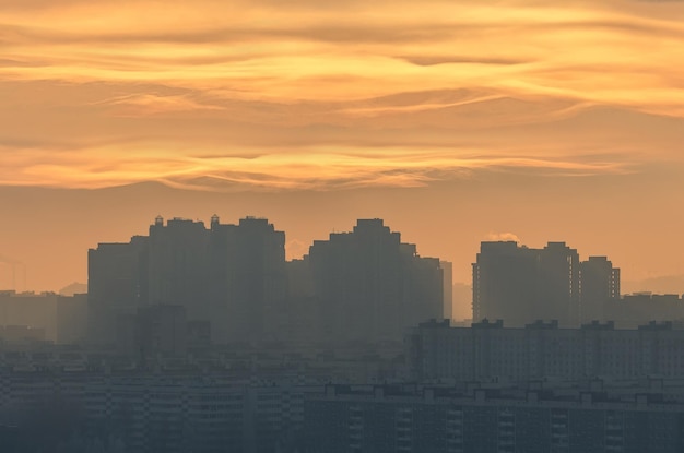 Silhouette einer urbanen Landschaft mit einer Sonnenscheibe, die durch niedrige Faserwolken einer verschmutzten urbanen Atmosphäre scheint