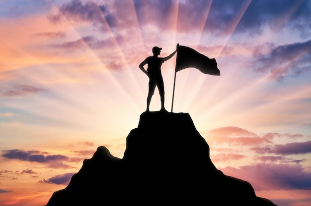 Foto silhouette eines bergsteigers mit einer flagge auf dem gipfel des berges, den er unterwarf. konzeptionelle szene