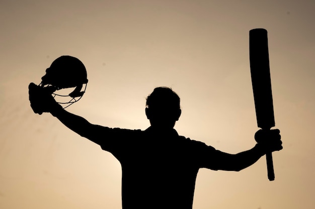 Foto silhouette eines cricket-spielers feiert, nachdem er in einem cricket-match ein jahrhundert gespielt hat.