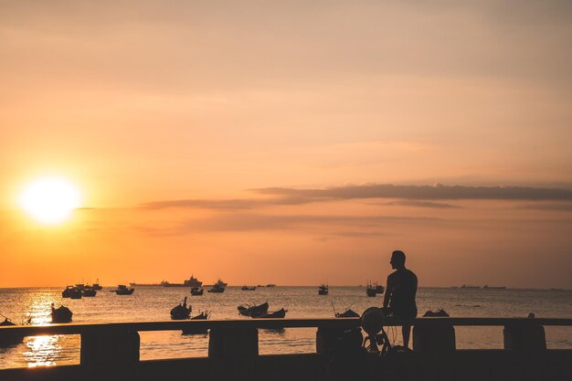 Silhouette eines depressiven jungen Mannes, der bei Sonnenuntergang vor einem tropischen Strand sitzt