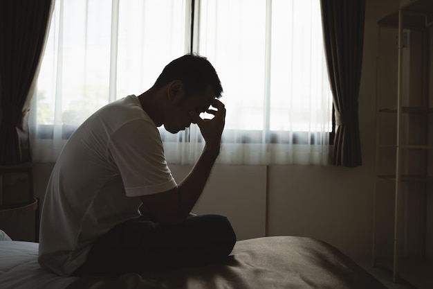 Silhouette eines depressiven Mannes, der traurig auf dem Bett im Schlafzimmer sitzt Traurige Männer, die an Depressionen leiden