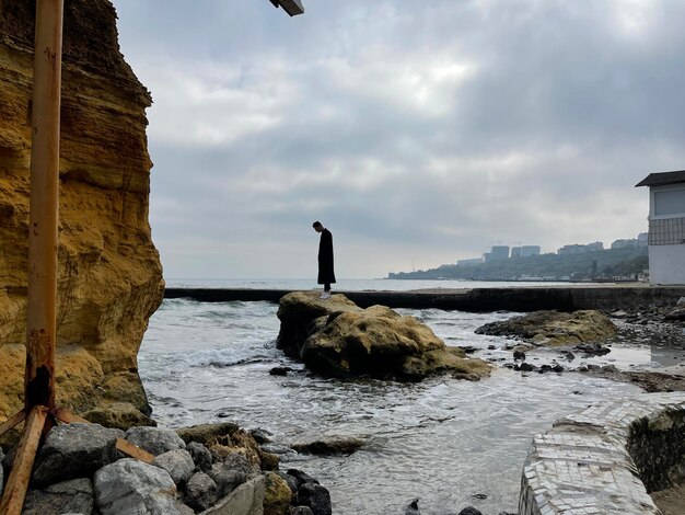 Silhouette eines einsamen Mannes, der auf einem Stein im Meerwasser steht