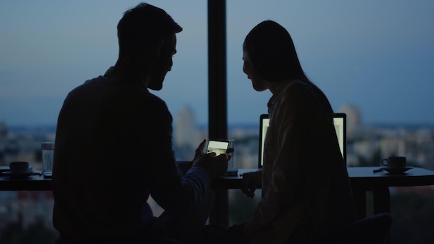 Silhouette eines entspannten Paares, das sich im Büro Videos auf dem Handy ansieht