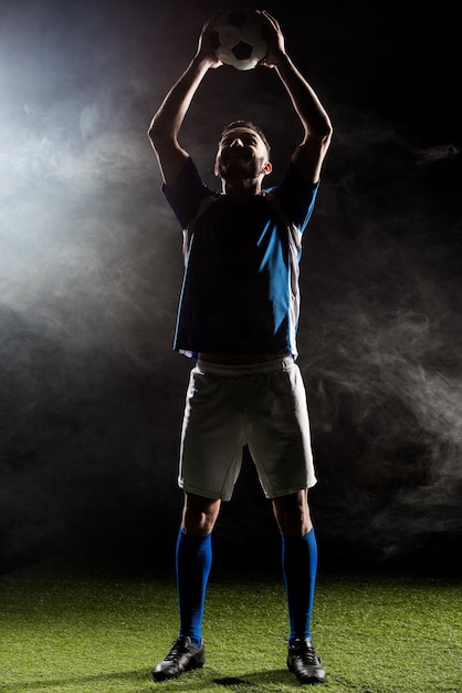 Silhouette eines Fußballspielers, der den Ball über dem Kopf auf schwarz mit Rauch hält