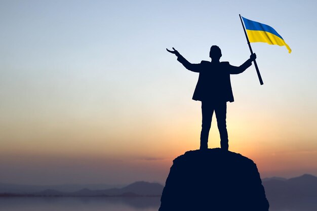 Silhouette eines Geschäftsmannes, der die Ukraine-Flagge mit Sonnenaufgangshintergrund hält