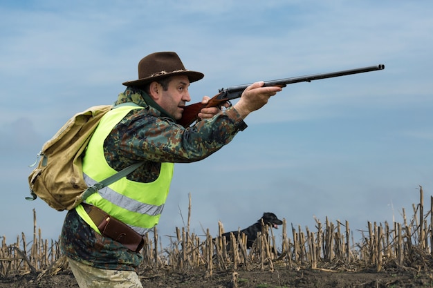 Silhouette eines Jägers mit einer Waffe im Schilf gegen die Sonne ein Hinterhalt für Enten mit Hunden