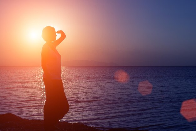 Silhouette eines jungen Mädchens, das in die Ferne blickt und bei Sonnenuntergang am Strand gegen die Sonne steht