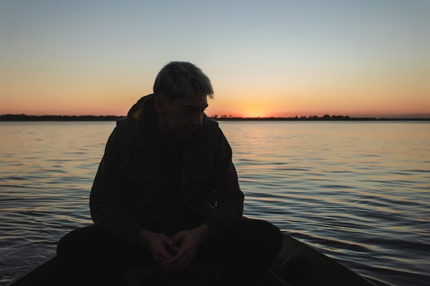 Silhouette eines jungen Mannes, der in einem Boot mit dem Sonnenuntergang im Hintergrund reitet.