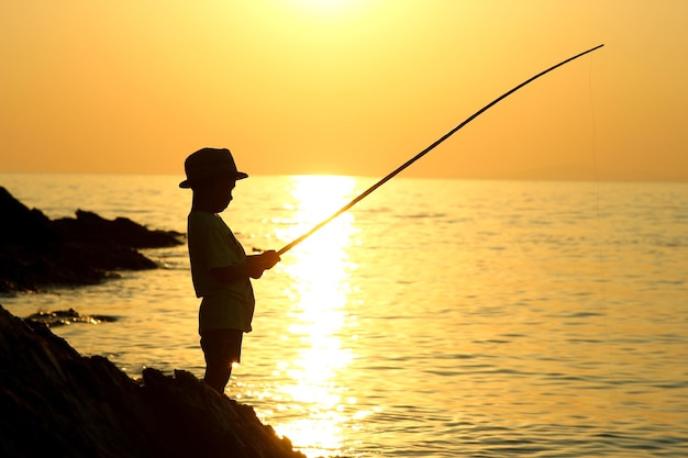 Silhouette eines Jungen mit einer Angelrute auf dem Meer